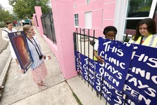  - 
              In this April 15, 2013 photograph, abortion opponent Corrie Zastrow, left, calls out to patients while clinic escorts secure signs on the front gates to prevent abortion opponents from 