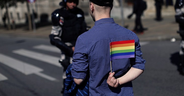 A gay activist holds a Peace flag as he stands in front of members of the Serbian Gendarmerie during the Pride March in Belgrade, Serbia, Sunday, Sept. 28, 2014. Thousands of anti-riot