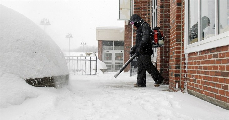 Brian Murphy uses a leaf blower to remove snow from in front of a store entryway Monday, Feb. 9, 2015, in Sudbury, Mass. A long duration winter storm that began Saturday night remains i