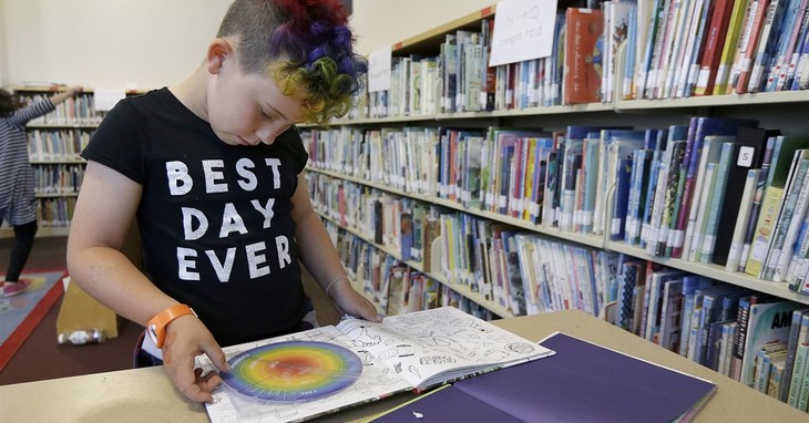 Image shows child with colored rainbow hair in a library reading a book. Shirt says Best Day Ever. Book Bans containing LGBT+ and other sexual material are controversial. 